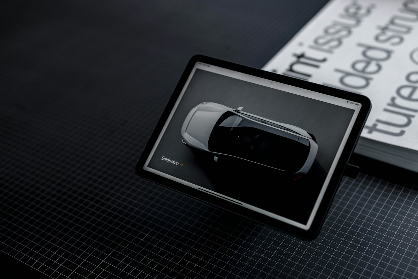 Tablet mit 3D-Auto-Rendering neben einem weißen Buch.