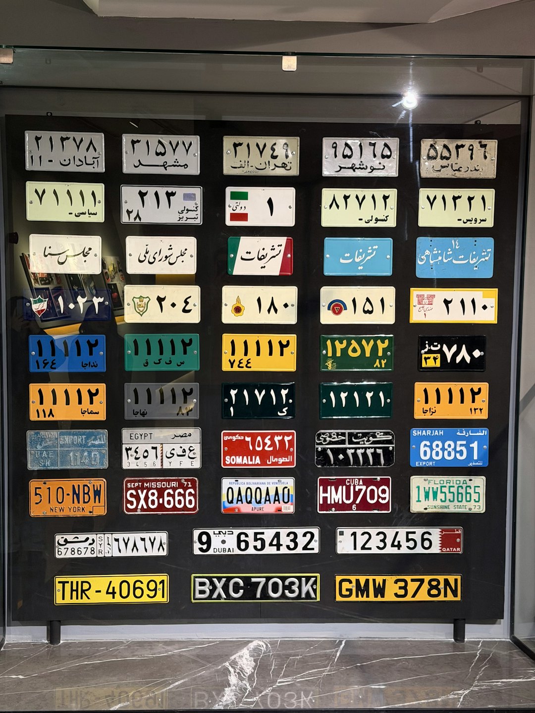 Internationale Nummernschilder in einem Gittermuster in einer Vitrine.